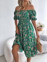 Donna con abito estivo verde a fiori, spalle scoperte, in posa accanto a un divano bianco. Moda femminile, abbigliamento estivo elegante.