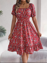 Donna con abito estivo rosso a fiori, maniche corte e scollo quadrato, in un ambiente moderno. Moda femminile, abbigliamento casual elegante.