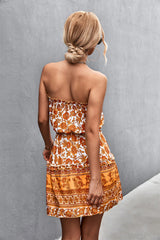 Donna di spalle con abito estivo floreale arancione, capelli raccolti in uno chignon, sfondo grigio. Moda estiva, abbigliamento femminile elegante.
